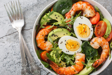 Balanced breakfast salad with shrimp, avocado, arugula, spinach, tomatoes and boiled eggs close-up...