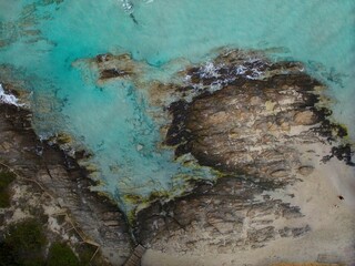 Picture from drone captures rocky coast of La Pelosa Beach, Sardinia, Sassari province. Sandy shore, turquoise water, and vegetation near the beach.