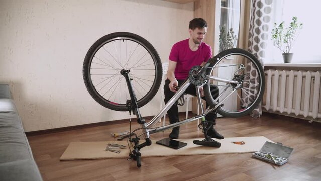Caucasian man turns pedal of bicycle and listens to extraneous sounds from creaking after home repare. Cyclist repairs his overturned mountain bike. Preparing for summer cycling season.