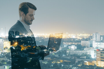 Attractive young european businessman using laptop while standing on night city background....