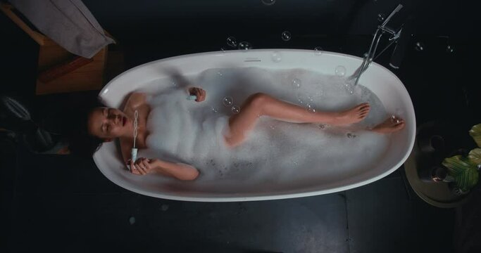VERTICAL VIDEO POV View from above on happy relaxed African American young woman enjoying bath and blowing soap bubbles.