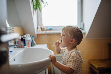Fototapeta premium Toddler brushing teeth in the morning, on his own. Morning dental hygiene for toddlers.