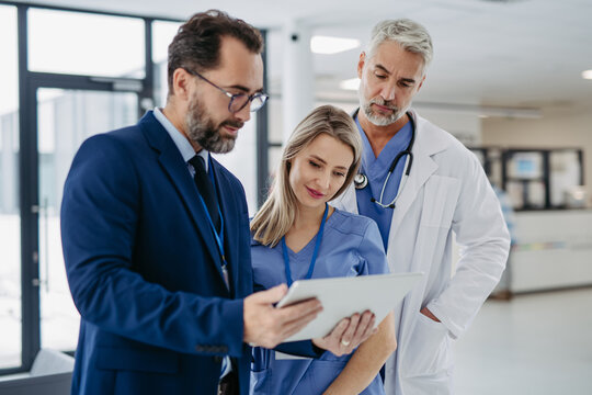 Pharmaceutical sales representative talking with doctors in medical building, presenting new medication on tablet. Hospital director, manager in modern clinic with doctor and nurse.