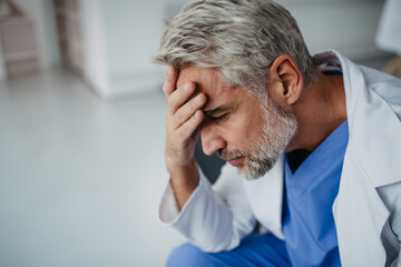 Side view of frustrated, exhausted doctor sitting in hospital corridor. Concept of burnout syndrome...