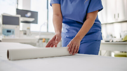 Nurse preparing examination table in emergency room, examination room. Discarding of used paper and...