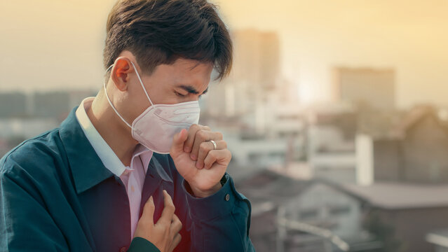 A young man wearing face masks to protect PM 2.5 smoke, city dust danger and air pollution in city, factory pipes and industrial smog. toxic mist. Protection against smoke. covid-19 protection. Fog.