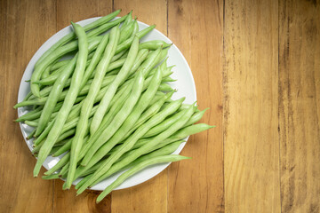 Fresh Bush bean or Fresh green beans on a white plate on wooden table.