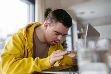 Young man with down syndrome learning online at home, using laptop. Telehealth consultation with...