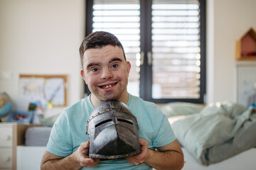 Portrait of smiling man with down syndrome at home, holding knight's helmet.