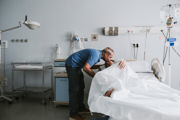 Man kissing woman lying on bed in hospital