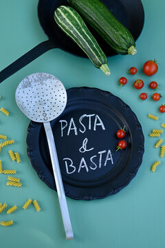 Studio shot of vegetables, pasta, sieve, frying pan and black plate with short phrase written in chalk