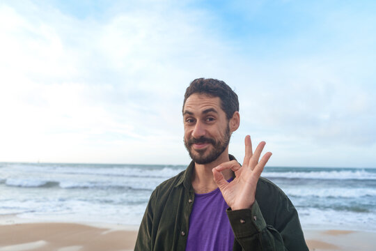 Smiling man gesturing OK sign in front of sea