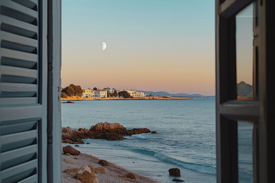 Fototapeta View through an open window with shutters, to see a sandy beach, rocky coastline, lovely small town and beautiful night sky with big, silver fully moon at blue hour...