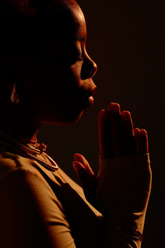 Woman with hands clasped standing against black background