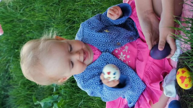 Vertical video. Baby with older sister having egg tapping while sitting on the grass outdoors, slow motion