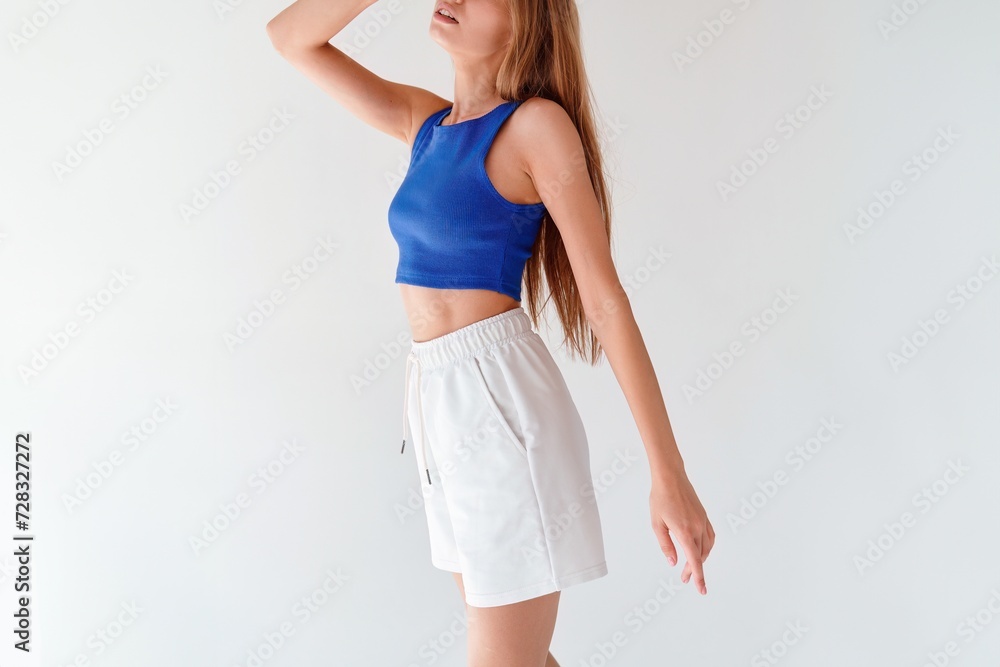 Wall mural A woman in a blue crop top and white shorts confidently poses in a studio with natural lighting and a light background. Summer lothing mock-up for branding and logos - Wall murals