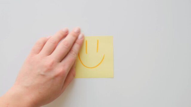 A hand sticks a piece of paper with a hand drawn smiling face