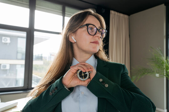 Businesswoman with wireless in-ear headphones holding compass at office