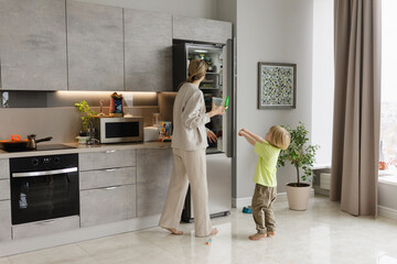 Woman standing near refrigerator with son in kitchen at home