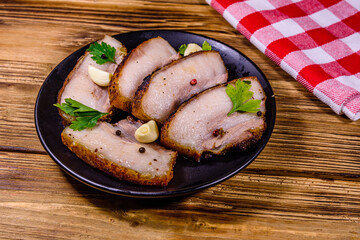 Slices of baked pork belly, garlic and parsley on a black plate