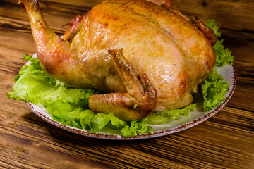 Plate with roasted whole chicken and lettuce leaves on a wooden table