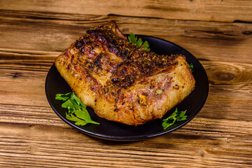 Baked piece of pork belly and parsley on a black plate