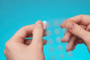 Close-up round acne patch on finger on blue background. Acne patches for treatment of pimple and...