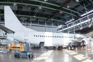 White passenger jetliner in the aviation hangar. Jet plane under maintenance. Checking mechanical systems for flight operations
