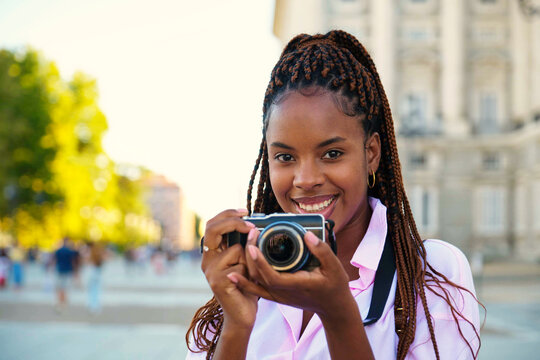 Black female tourist smiling and looking at camera while taking photos with a camera sightseeing in Madrid, Spain.