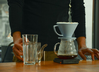 Professional barista making filtered drip coffee in coffee shop. Close up of hands barista brewing a drip hot espresso, pour over coffee with hot water and filter paper in cafe.