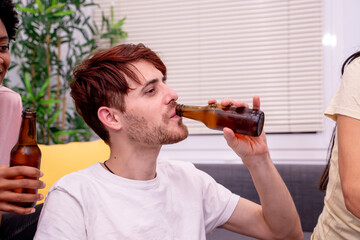 Tattooed man sips from a beer bottle with smiling friends in the background. 