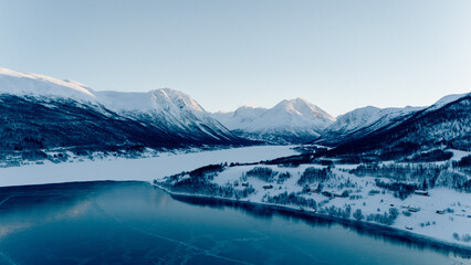 Aerial View over a Fjord in northern Norway during sunset with the sky reflecting in the water and the sun shining onto the peaks of the mountains