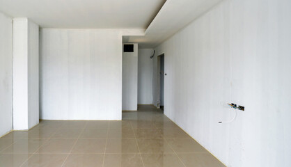 A bare white Primer color painted wall room with shiny marble tiled floor and lots of empty space. Unfinished room. Doors, service access panel and electrical outlet have not yet been installed.