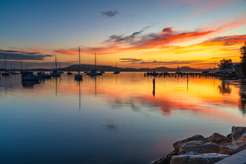 Sunrise with colourful cloud reflections and boats on the bay at Koolewong, NSW, Australia.
