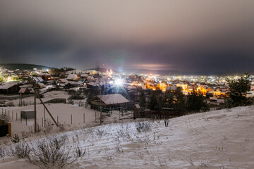 Mountain landscape with village in winter, houses and pine trees covered snow at night. Scenery of ski resort with lights. Theme of travel.