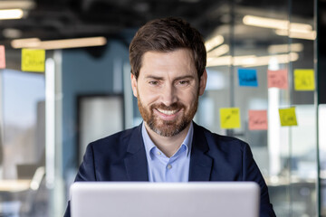 Successful satisfied businessman at workplace, boss in business suit typing on laptop keyboard,...