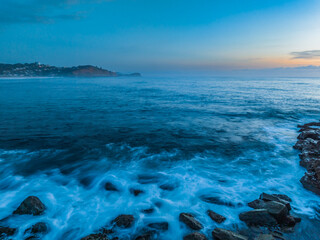 Fototapeta premium Sunrise over the calm ocean with light cloud and rocks