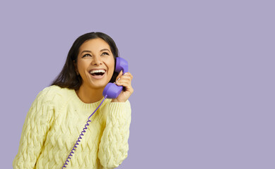 Funny joyful excited woman talking to friends using cable handset on pastel purple background....