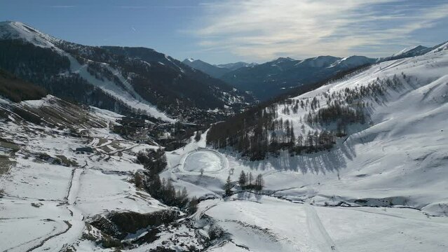 Vue a&eacute;rienne en drone de la station de ski de la Foux d'Allos, avec les montagnes enneig&eacute;es au dernier plan, et un lac artificiel gel&eacute; au premier plan.