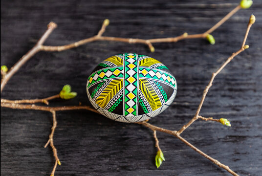Easter egg with green geometric ornament on a dark wooden background and spring twigs.