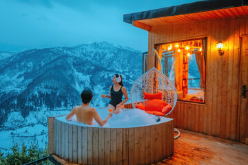 A couple enjoys a beautiful view of the morning snow in front of her room in a soaking tub at their...
