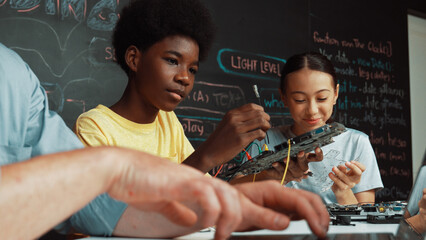 Young student fixing controller while teacher programing engineering code at STEM class. Closeup of...