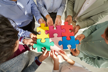 Group of business people assembling jigsaw puzzle, cropped shot. Office team putting pieces together searching for match, top view. Cooperation, help, support, teamwork concept