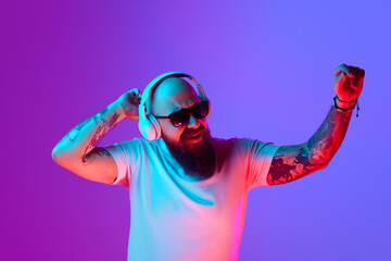 DJ. Bearded, artistic bald man with tattoos, in white t-shirt and sunglasses standing against...