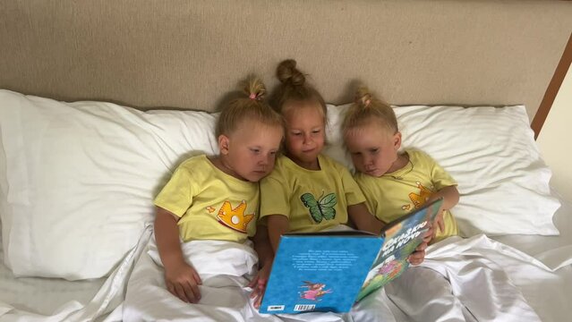 Triplets little girls, three sisters 3-4 years old, playing on the bed in pajamas, twins