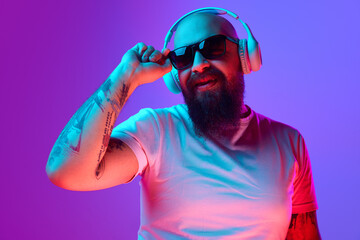 DJ. Bearded, artistic bald man with tattoos, in white t-shirt and sunglasses standing against...