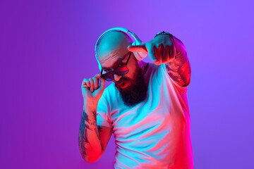 DJ. Bearded, artistic bald man with tattoos, in white t-shirt and sunglasses standing against...