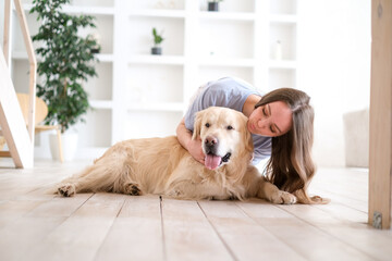 Portrait of happy young woman with pet dog sitting on floor at home. Caucasian female hugging golden retriever in living room