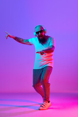Full-length image of bearded bald man in casual clothes, with tattoos, listening to music in...