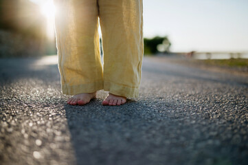 Close up of girl's barefoot legs in summer outfit on walk during summer vacation, yellow linen...
